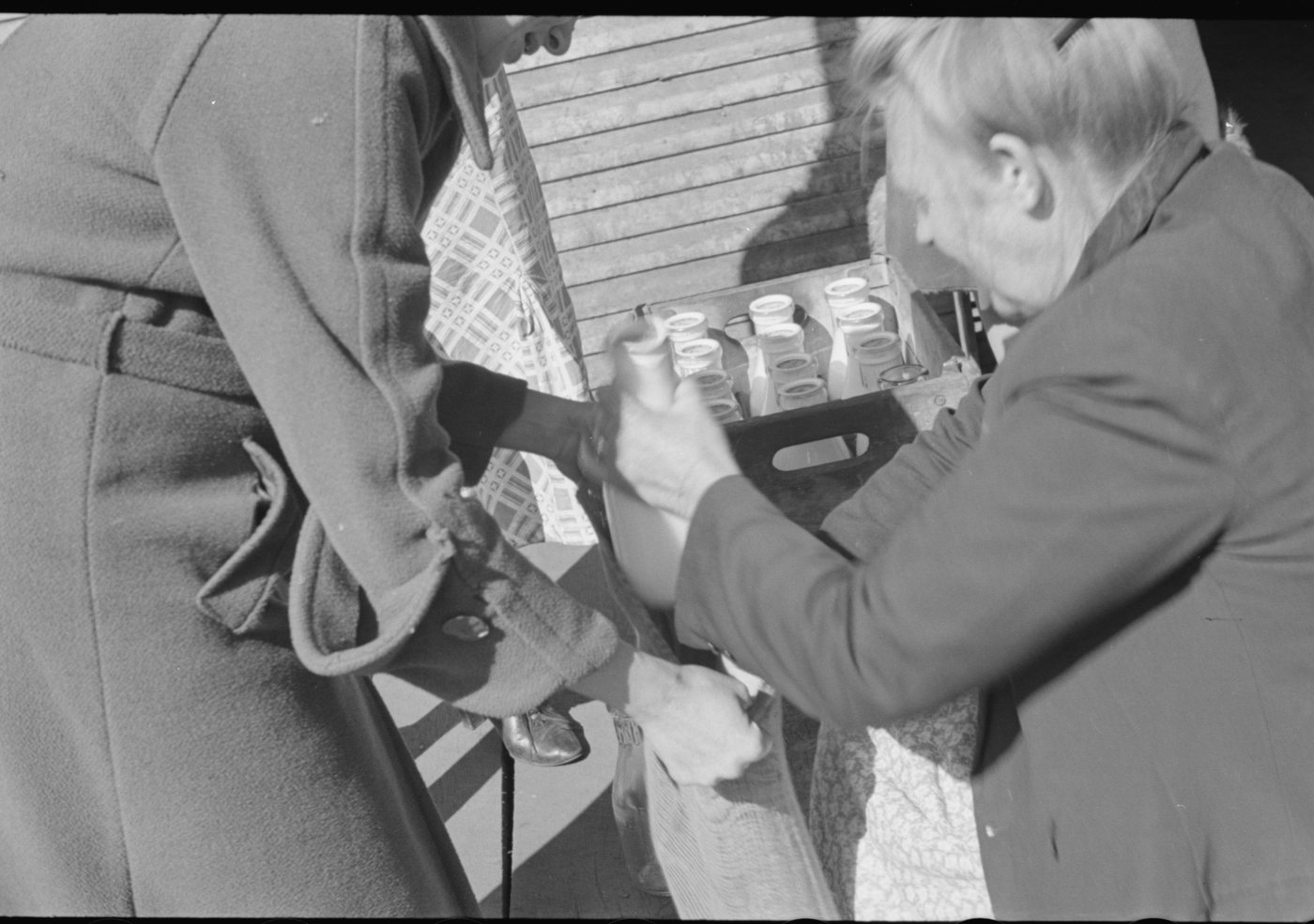 Two people bending over a crate of milk bottles at a relief station