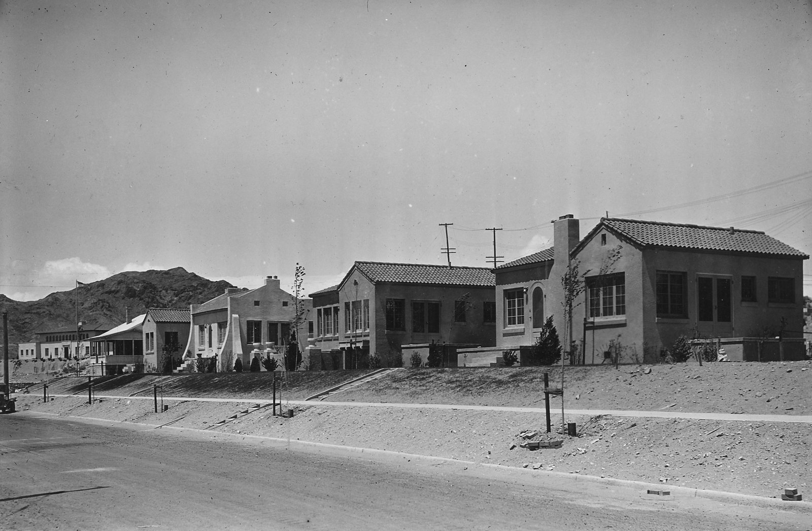 A row of stuccoed houses with tiled roofs and young lawns along a paved street