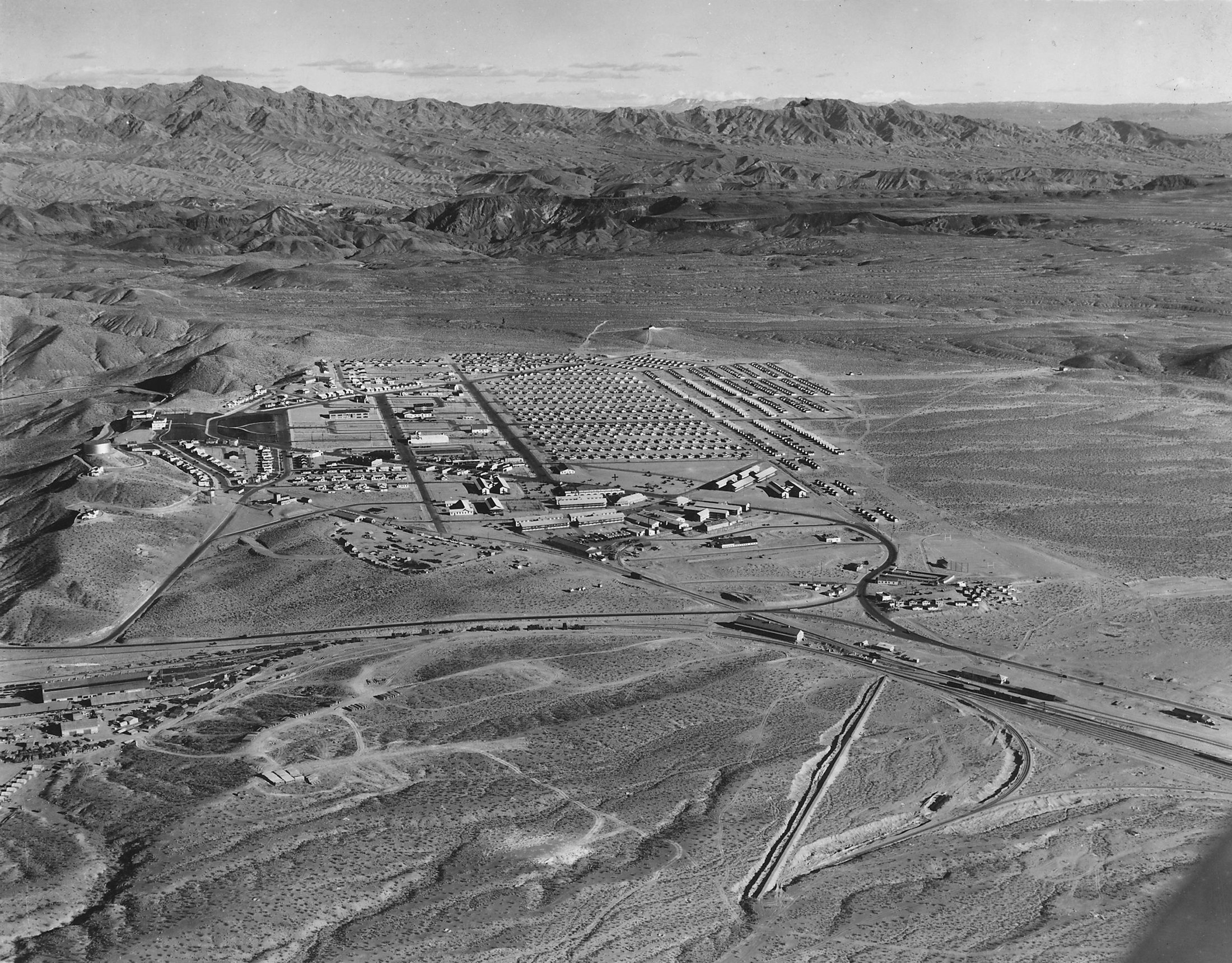 An aerial view of a new town laid out in a fan of streets on bare desert, with mountains beyond: Boulder City, December 1932