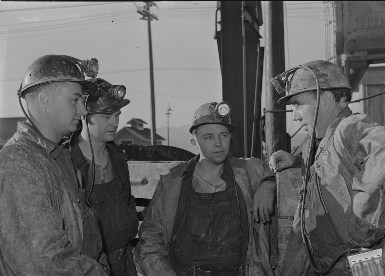 Four miners in helmets and lamps standing at the mine head