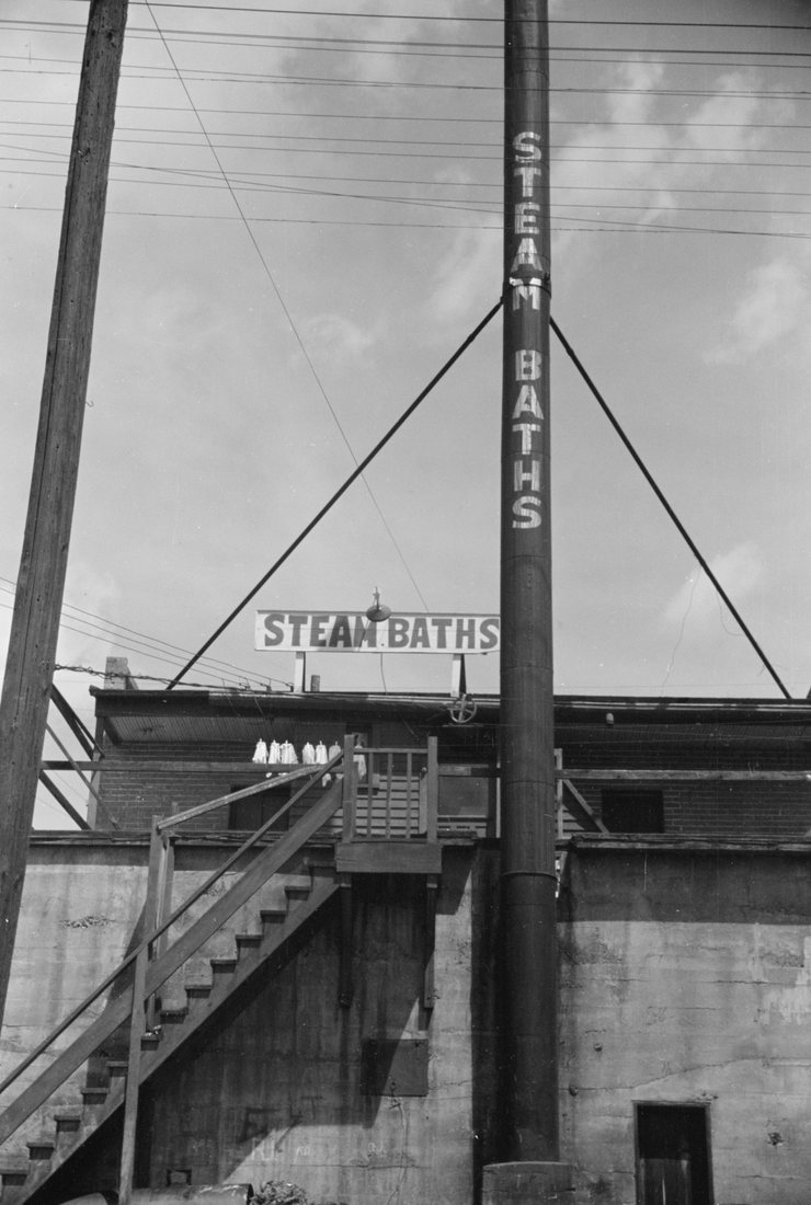 A tall stack lettered STEAM BATHS above a concrete building with an outside stair
