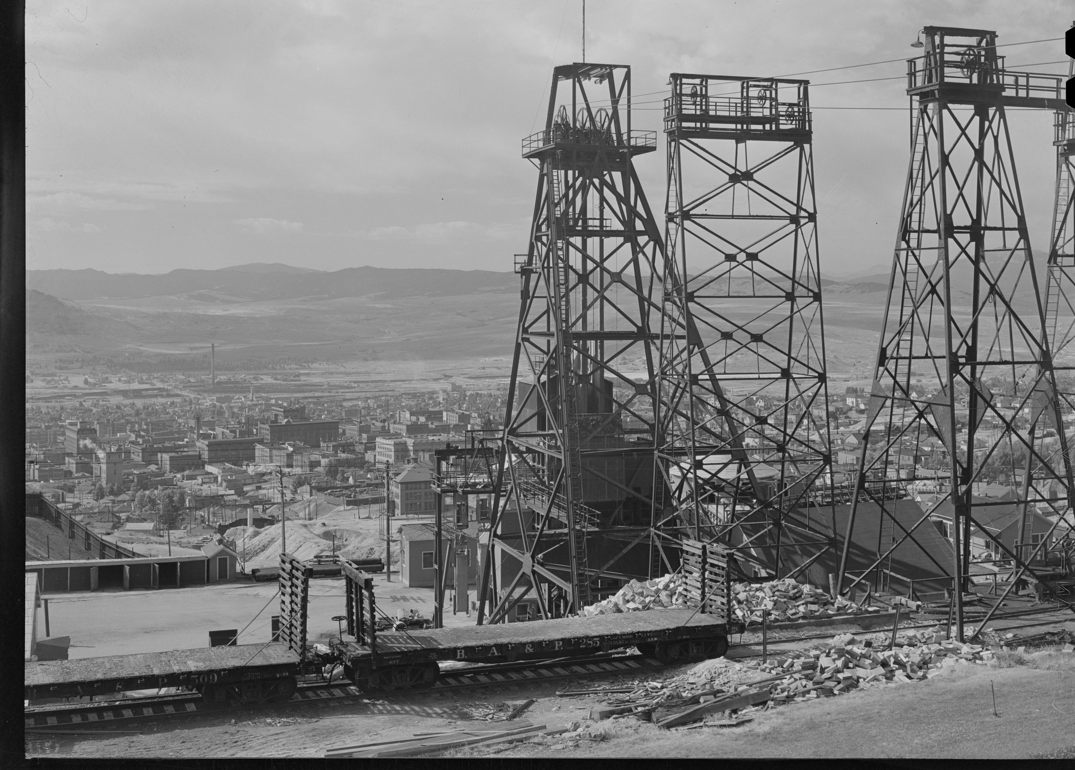 Steel headframes of copper mines on a hillside above the town of Butte, mountains beyond, 1942