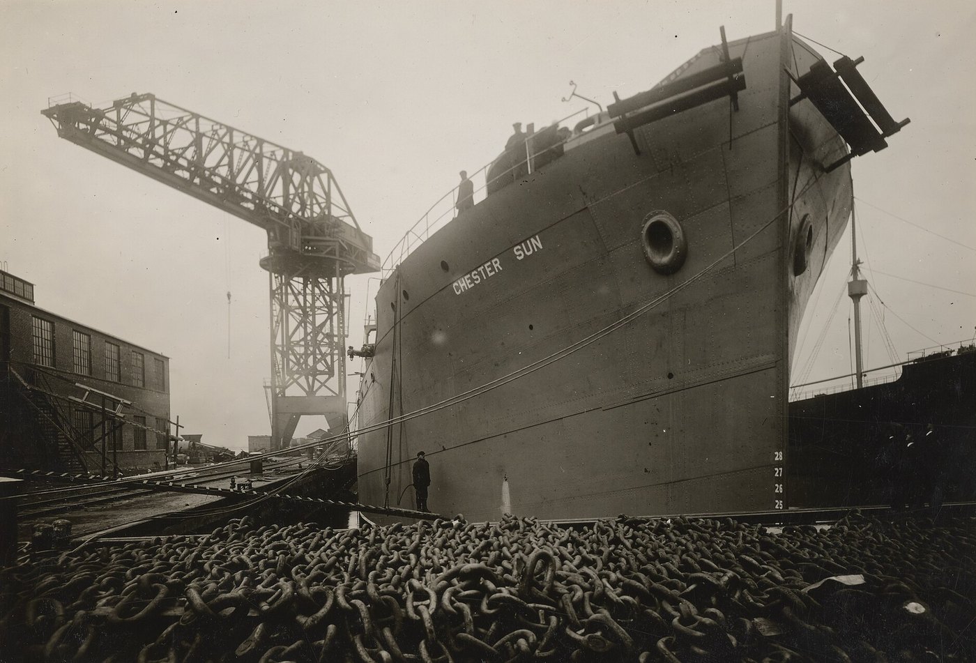 The tanker Chester Sun fitting out beside a hammerhead crane, with anchor chain piled in the foreground, Chester, December 1917