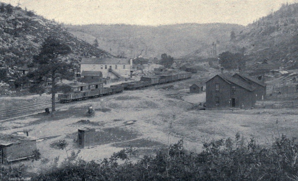 A railway siding with coal cars and a two-storey company building in a narrow canyon