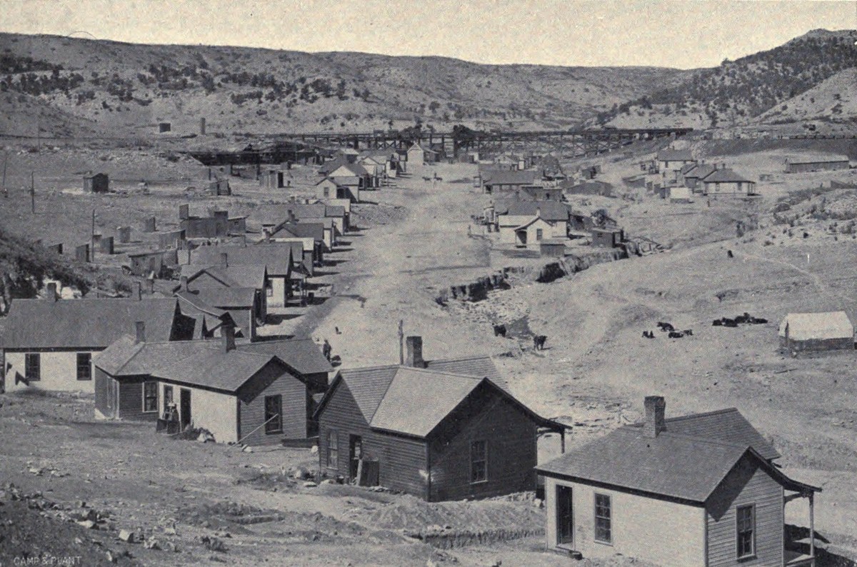 Rows of small frame company houses climbing a bare valley floor, a canyon wall behind