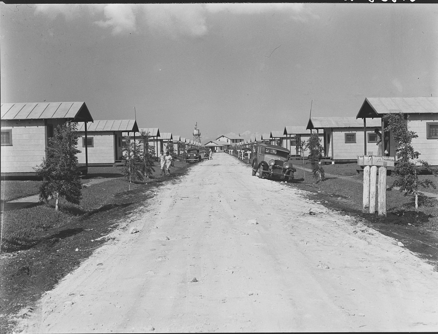 Two rows of identical small white houses on either side of a straight sandy road