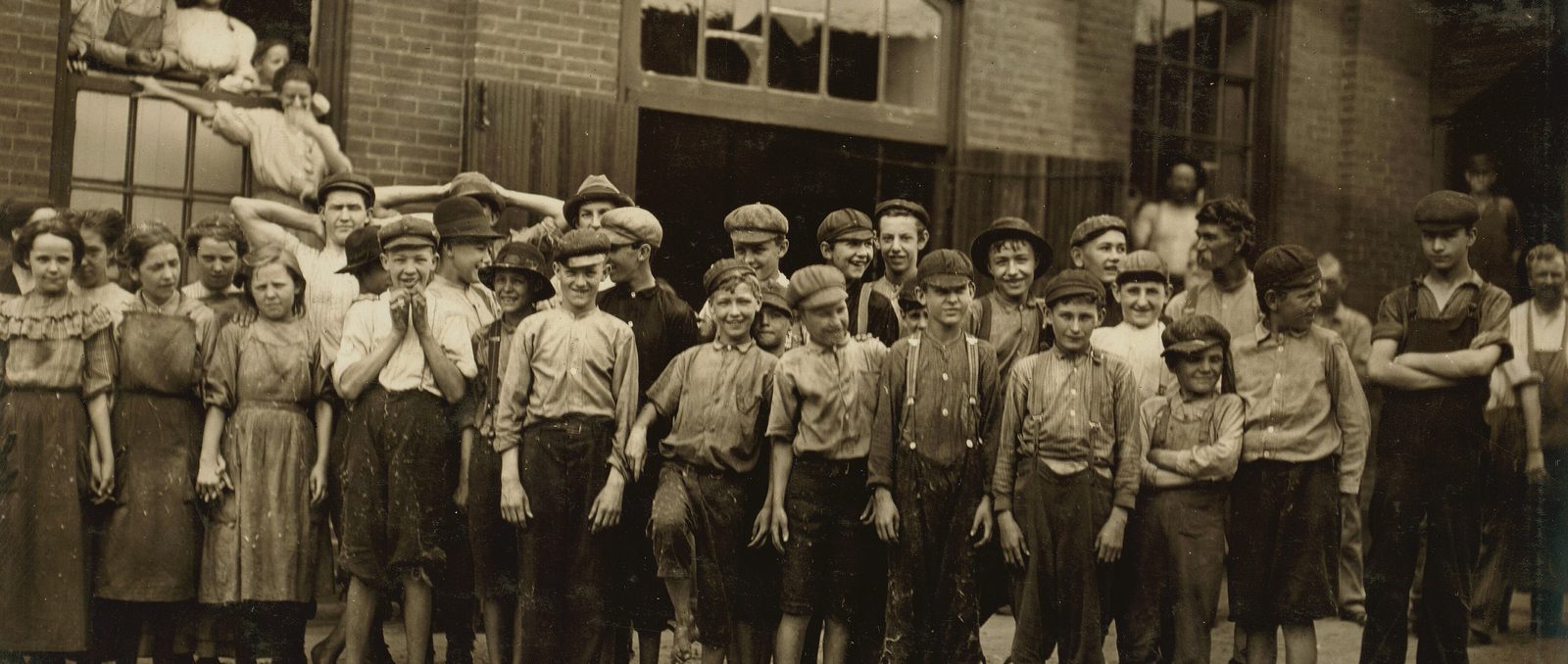 A crowd of mill workers, many of them children, standing in front of a brick mill door at the noon hour, Riverside Cotton Mills, Danville, 1911