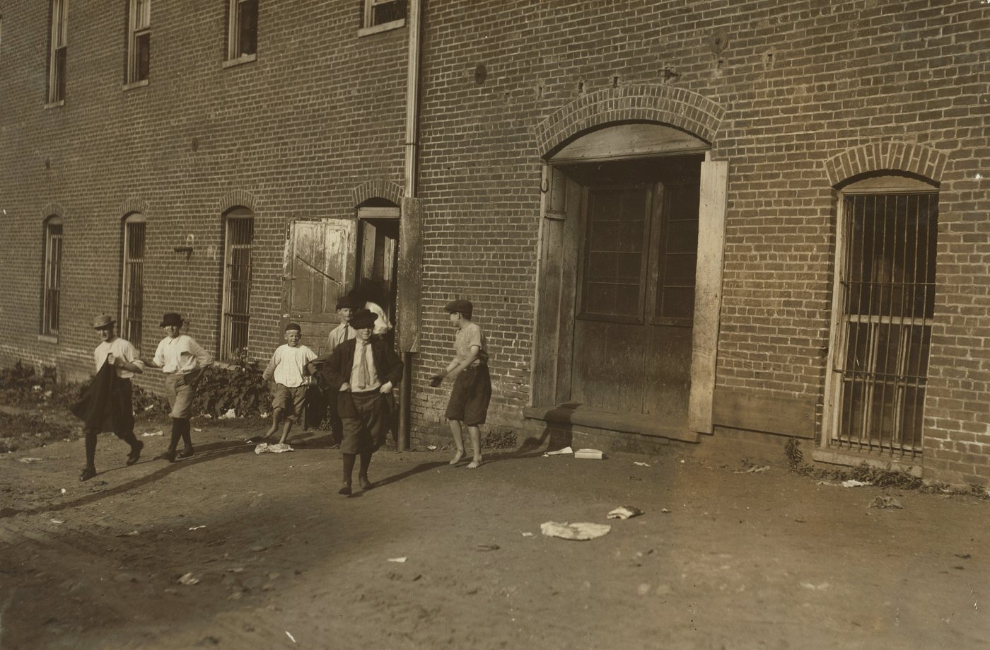 Children and young people walking away from the arched doorway of a brick factory into a dirt street