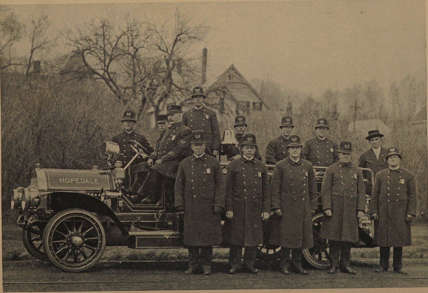 A dozen uniformed policemen standing on and beside a motor fire engine marked Hopedale