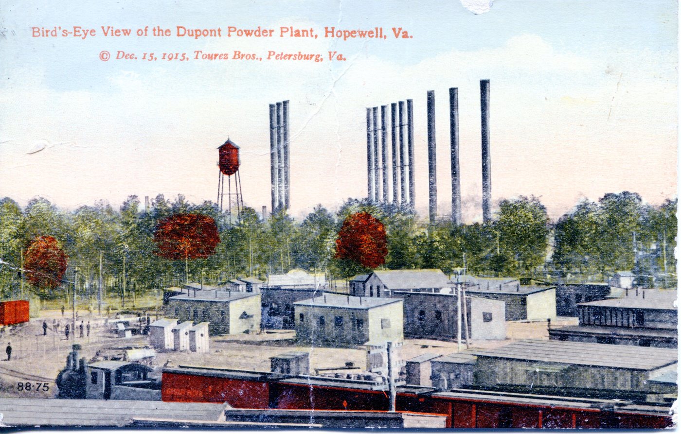 A hand-coloured postcard of the DuPont powder plant at Hopewell: rows of low buildings, a water tower and a line of tall stacks