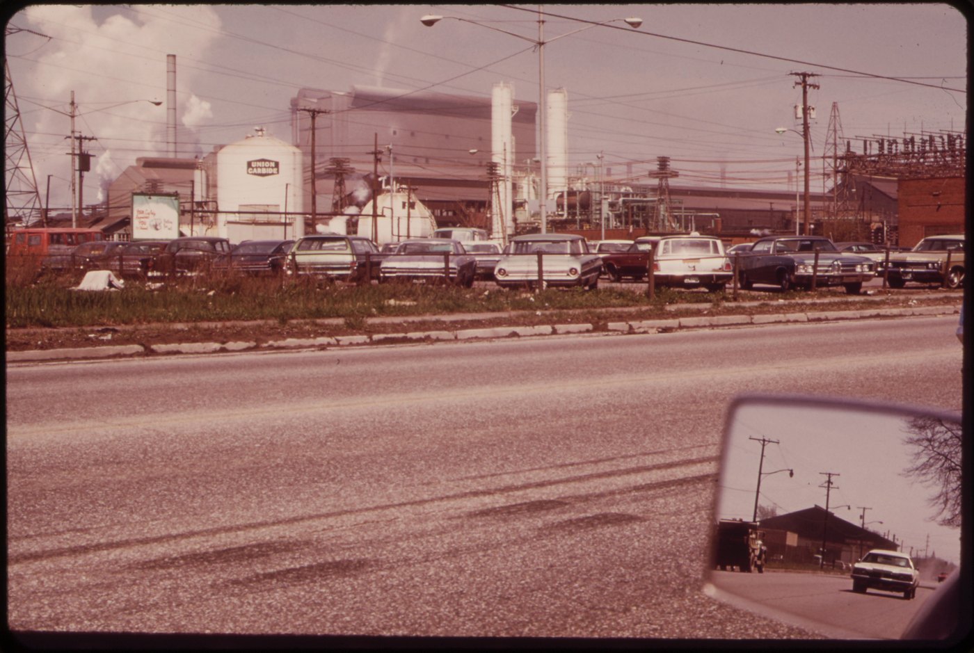 Smoke rising from the U.S. Steel plant at Lorain behind a parking lot of 1970s cars, April 1973