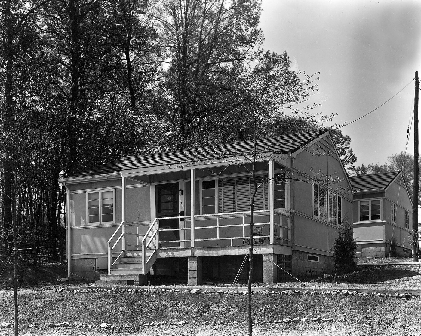 A small single-storey house with a porch and steps, set among tall trees