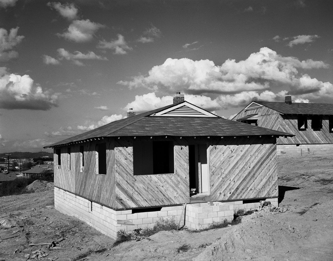A small new house of diagonal timber boarding on a concrete-block base, on raw graded ground under a cloudy sky