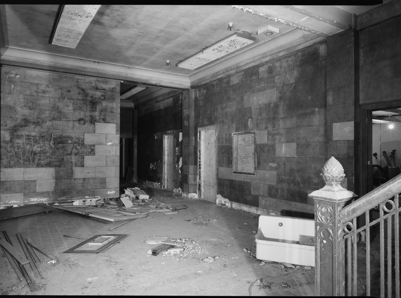 A wrecked office lobby with marble walls, debris on the floor and an ornate stair newel post