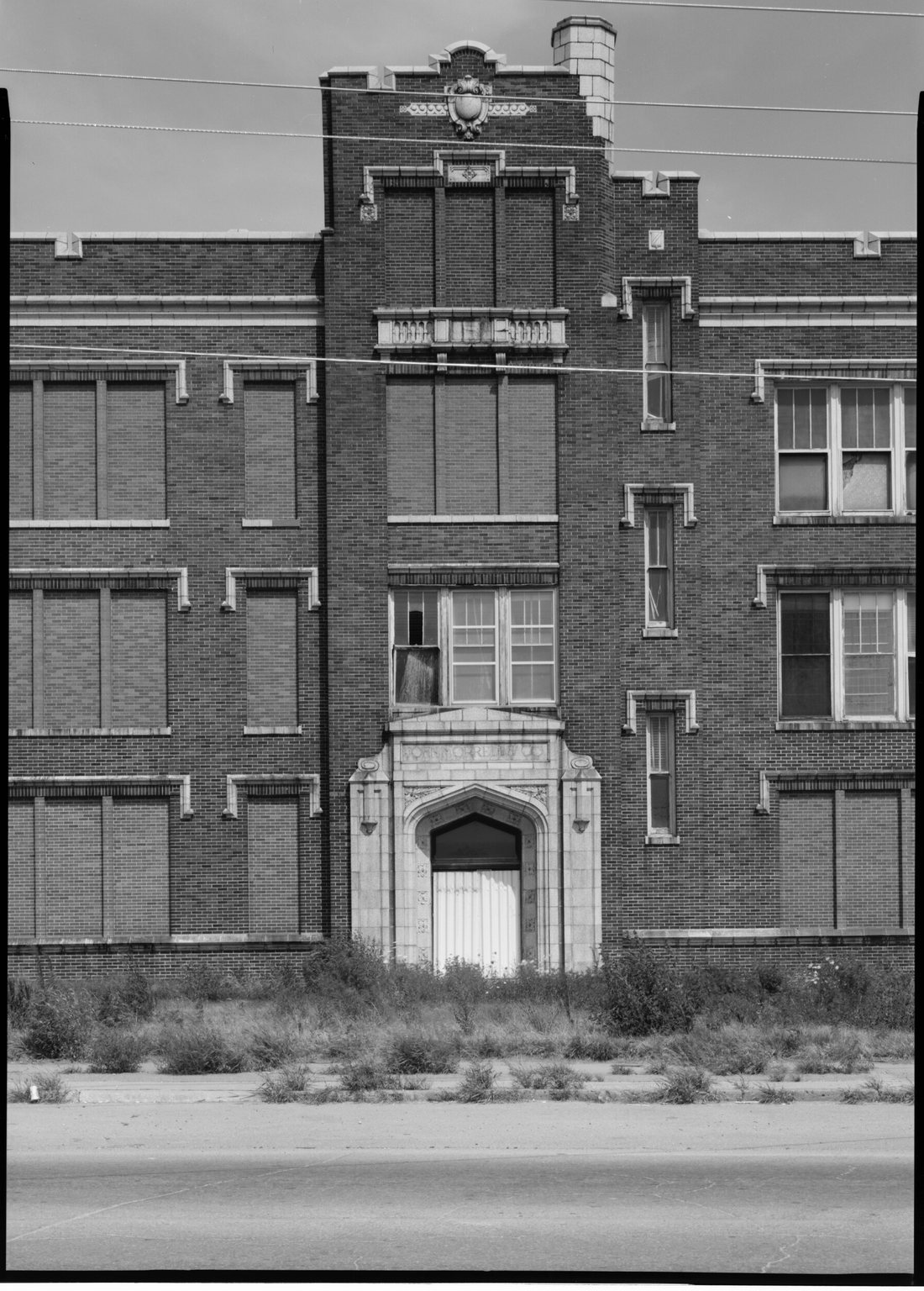 The tall brick tower and stone entrance of an office building, its windows boarded