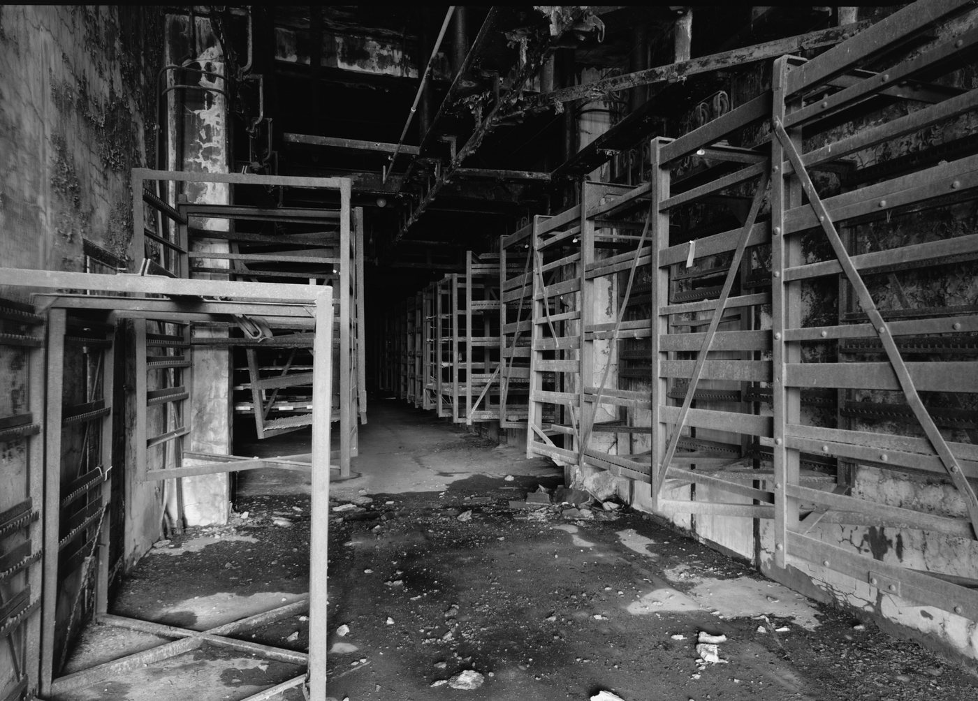 Rows of tall wooden and steel racks along a dark corridor with a debris-strewn floor