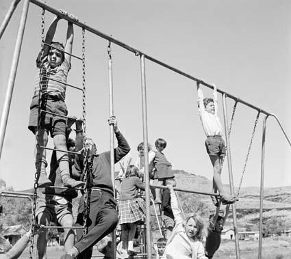 Children climbing on a metal playground frame with ladders and swings, hills behind